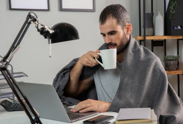 Hombre tomando café mientras trabaja desde casa con su laptop.<br />