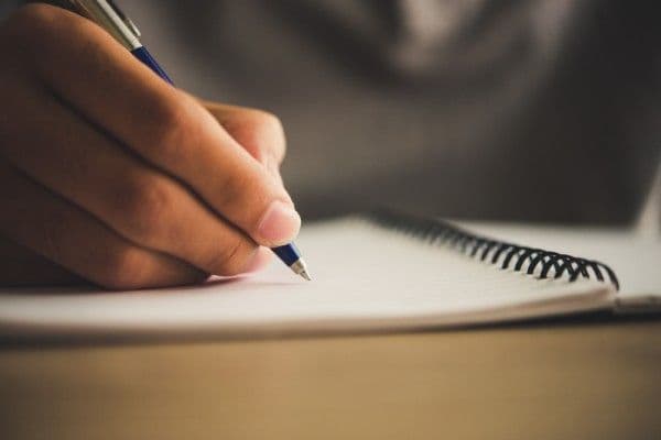 Primer plano de persona anotando en un cuaderno de asistencia.