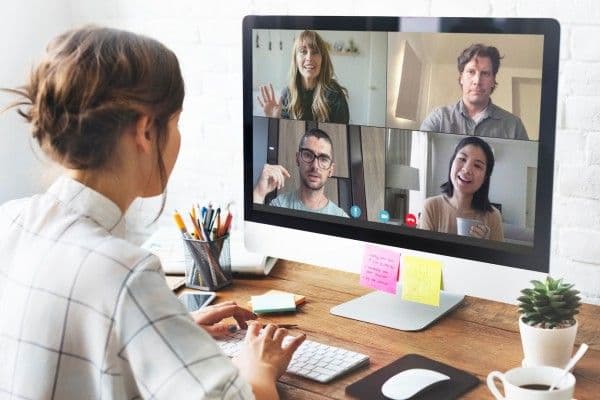 Mujer trabajando desde su casa mientras realiza videoconferencia con cuatro personas.