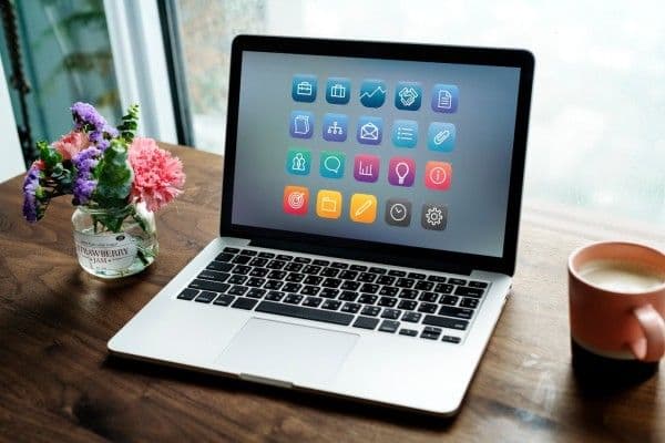 Computador portátil puesto sobre un escritorio, donde además hay una taza con café y un florero.