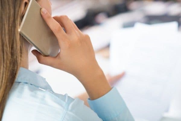 Primer plano de mujer hablando por teléfono inteligente y sosteniendo papeles.<br />
