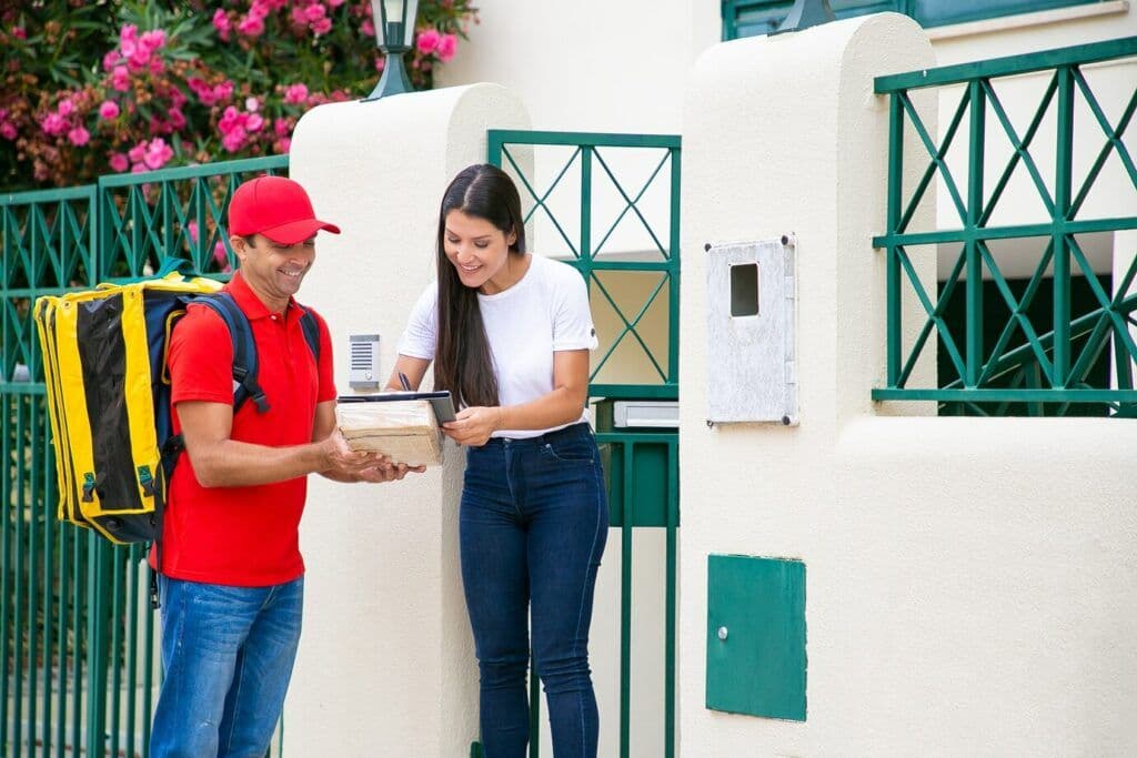 Cliente mujer firmando la hoja de entrega con lápiz. mientras mensajero tiene un paquete en sus manos.