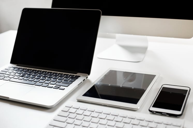 Ordenador portátil, junto a una tableta inteligente y un teléfono inteligente. Todos con carcasa de color blanco y puestos sobre un escritorio.