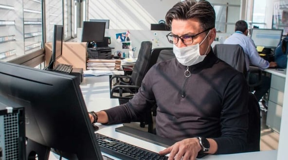 Trabajador con mascarilla, durante la pandemia COVID19, utilizando su ordenador de mesa en la oficina,