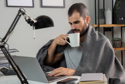 Hombre tomando café mientras trabaja desde casa con su laptop.<br />
