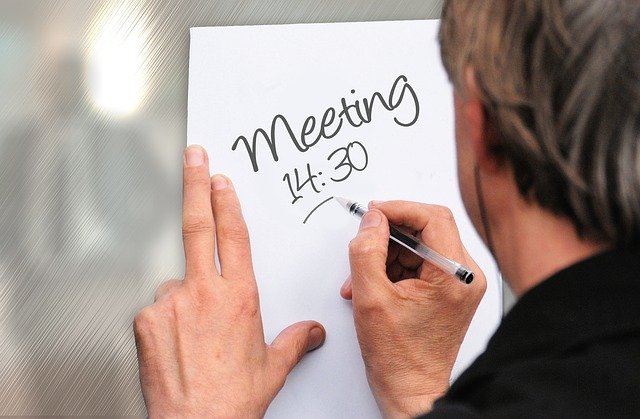 Persona escribiendo en una hoja de papel la hora para un meeting.