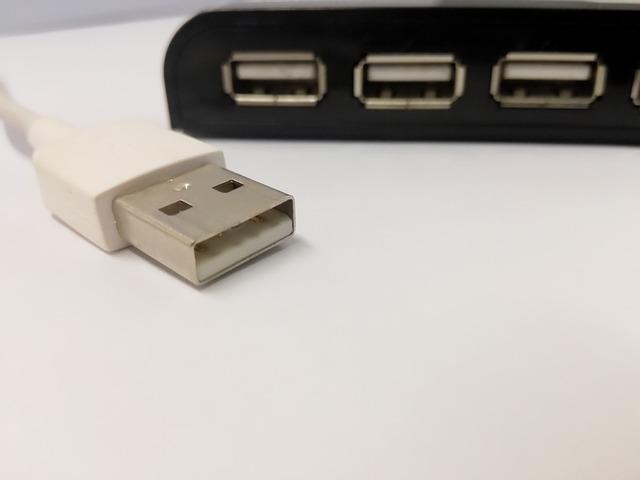 Cable usb sobre un escritorio blanco, junto a un dispositivo con varios puertos de este tipo.