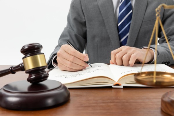 Hombre escribiendo sobre un escritorio con un mazo y una balanza de justicia, simbolizando la creación de una ley.