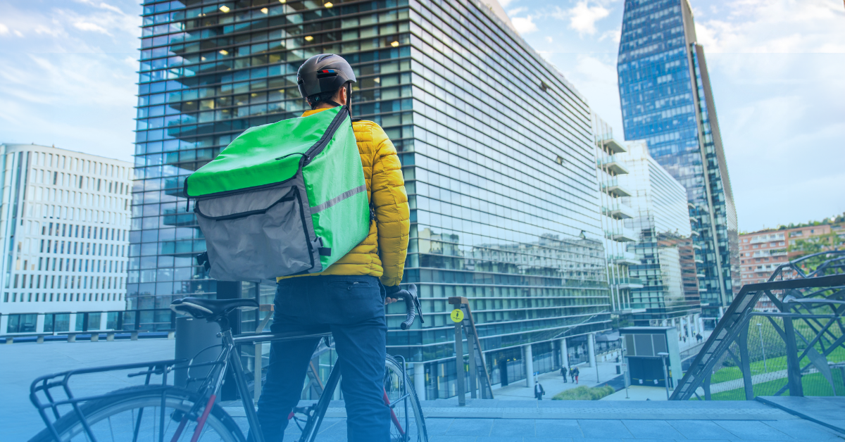 Domiciliario con bicicleta frente a zona empresarial moderna, simbolizando el trabajo de plataformas digitales en entornos urbanos bajo la nueva reforma laboral en Colombia.